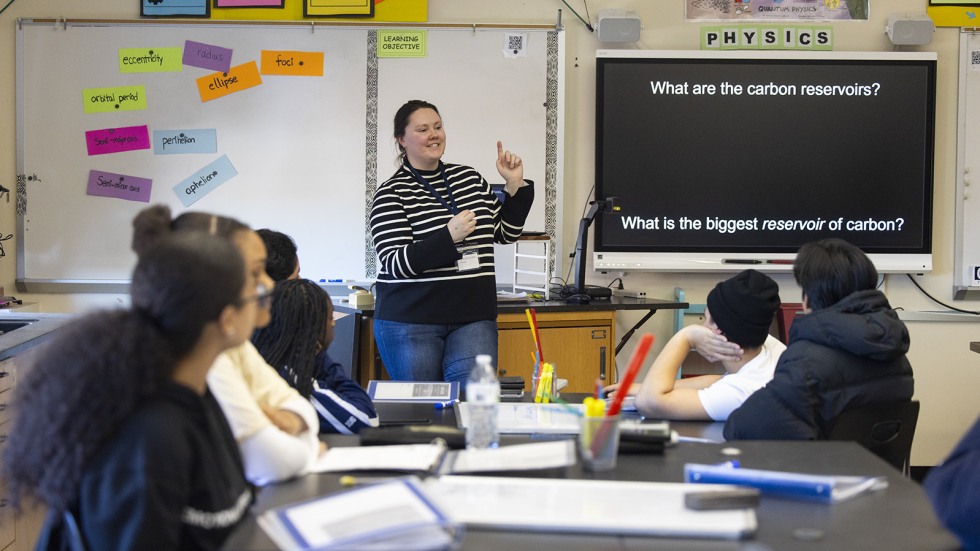 Brown graduate students leads a discussion among a table of high schoolers.