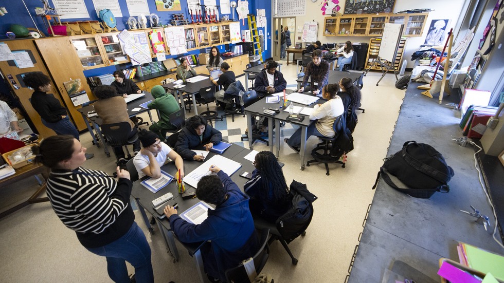 Brown graduate students leads a discussion among a table of high schoolers.