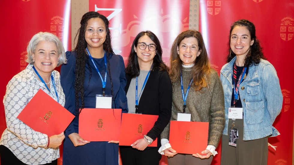 Five people pose for a photo against a red backdrop
