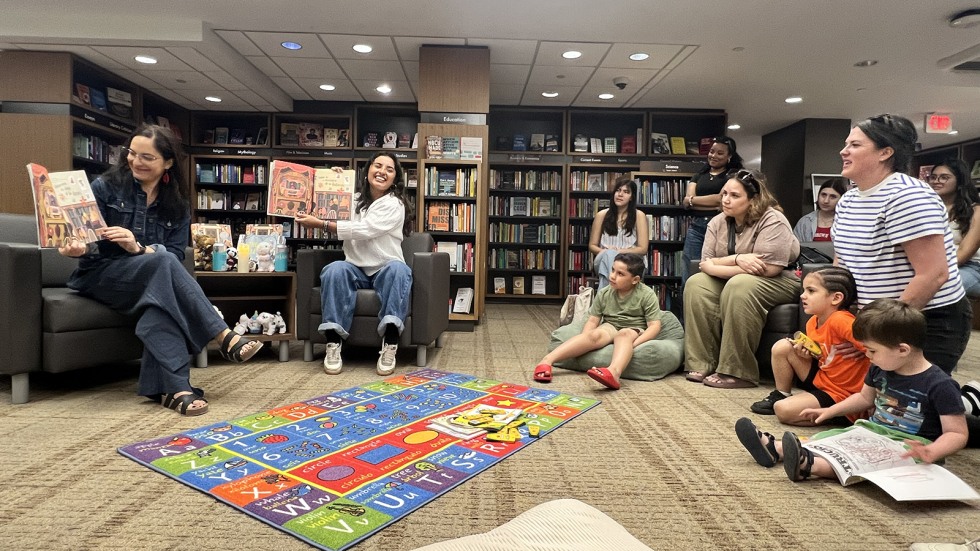 families gather in a circle for story time as readers sit in chairs holding picture book
