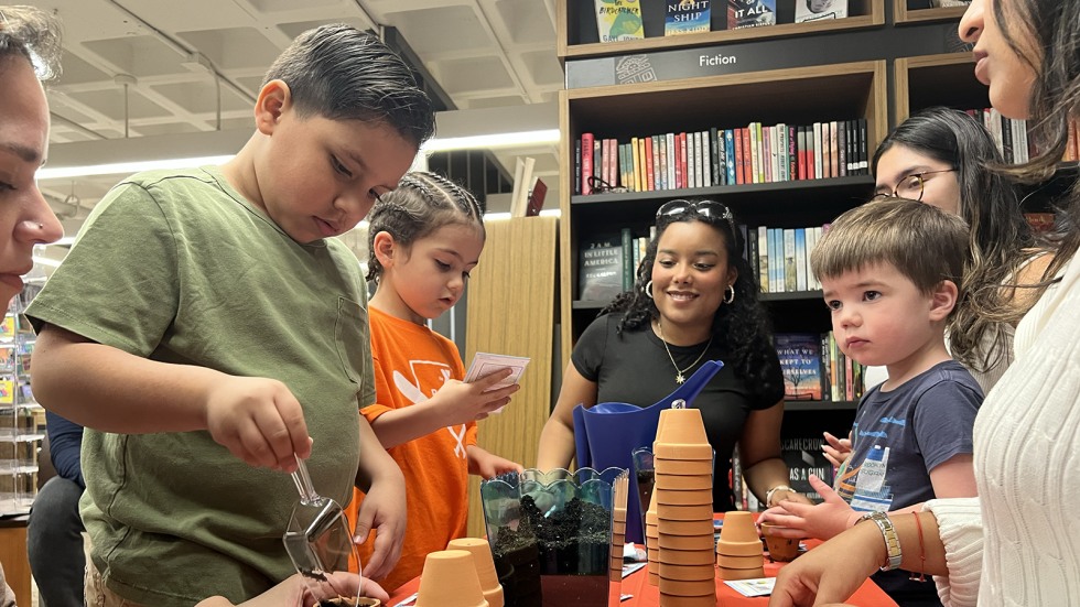 kids and Brown students work together to plant flower seeds in small clay pots