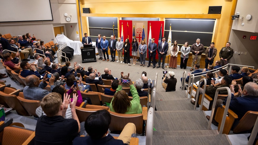 15 graduating veterans stand in front of a crowd receiving a round of applause