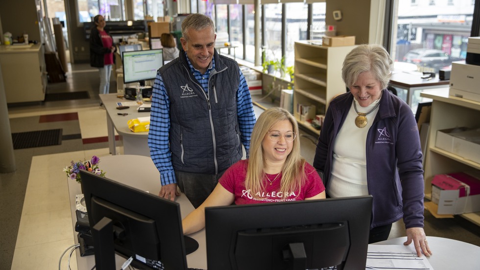 staff from family-owned print shop, Allegra, stand together working on a project in their headquarters