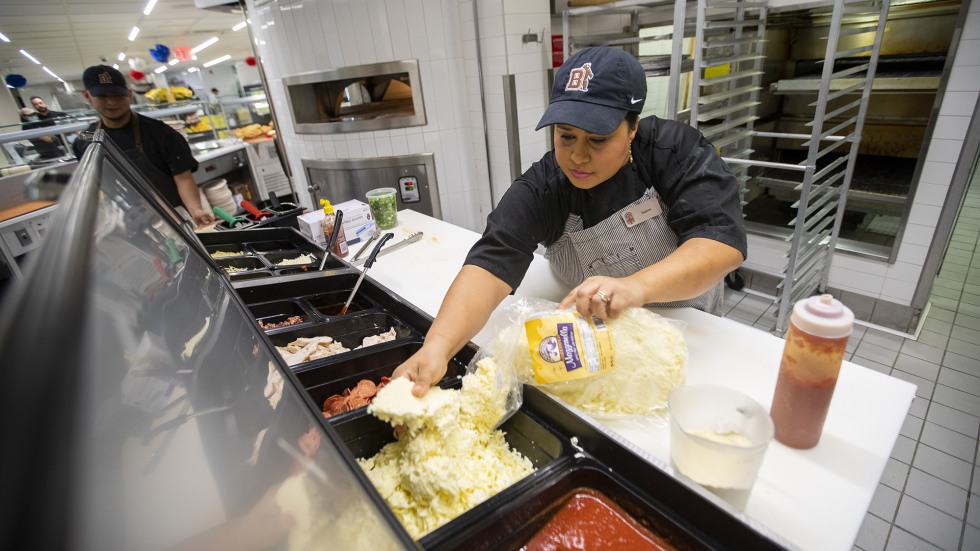 Dining services worker at Brown fills food station with mozzarella cheese