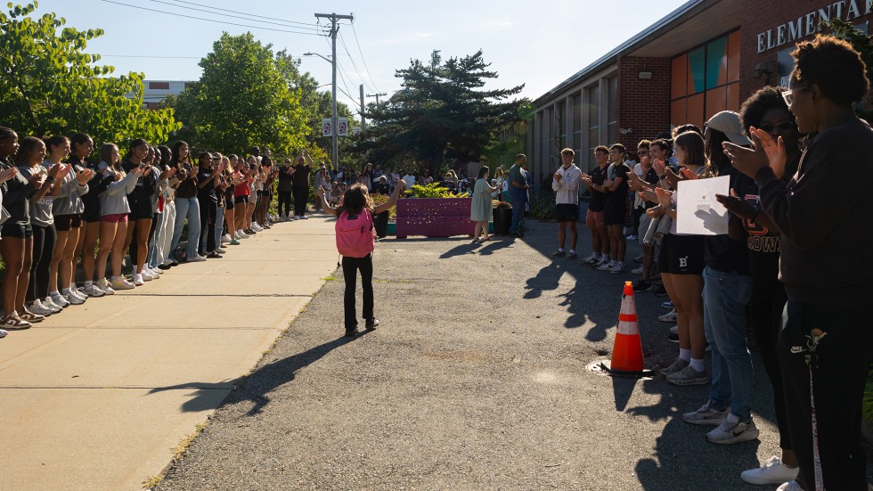 K-5 students are cheered on by student-athletes as they walk into the school building.
