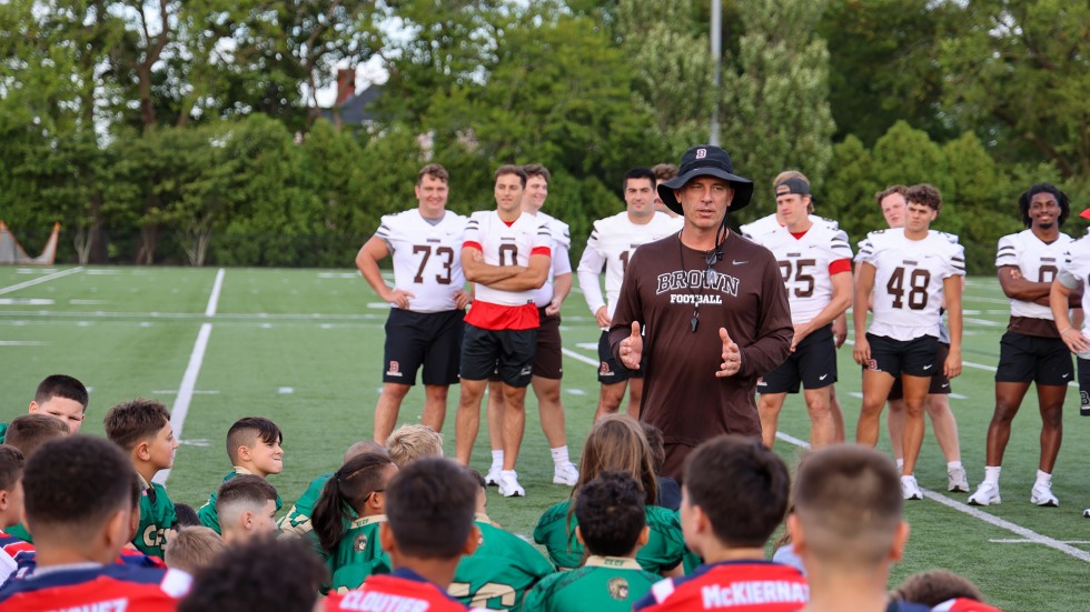 Brown football coach address group of kids attending the football clinic.