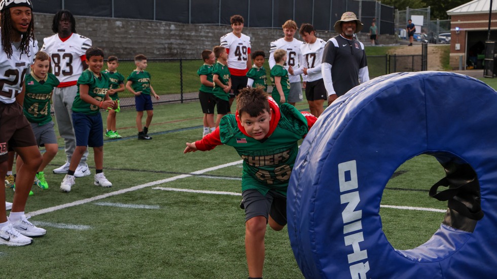 Young kids practice tackle drills, chasing a tackle wheel.