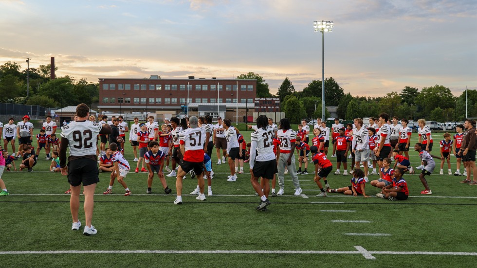 Hundreds of young kids join Brown football players on the field for drills.