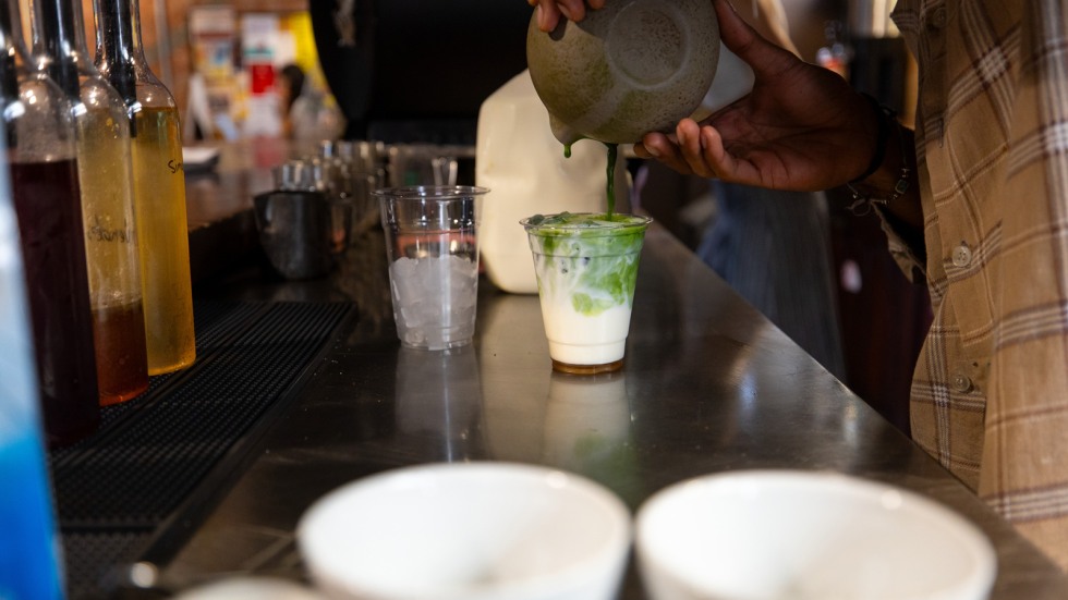 Barista pours matcha into an iced latte