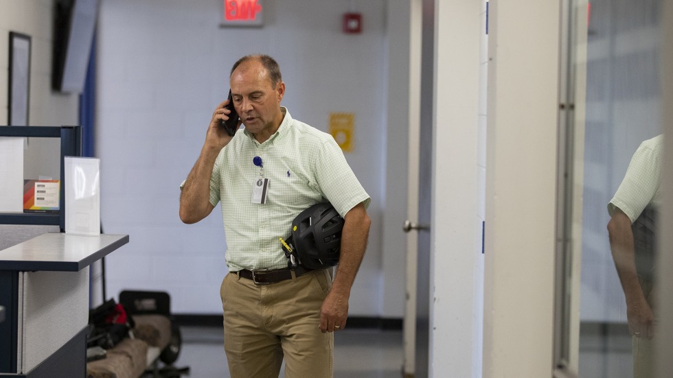 Brown staff member stops along a corridor in a campus building to take a phone call. 