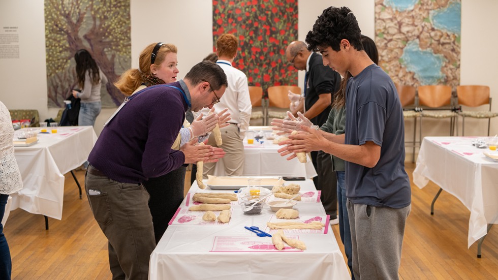 people standing around a table working with challah dough