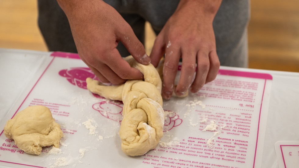 person braiding a challah loaf