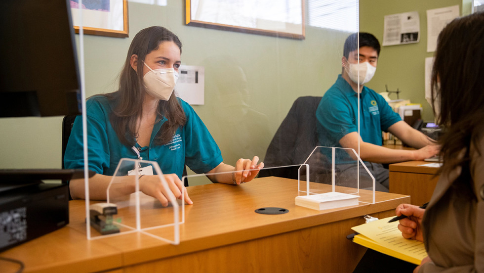 Brown medical students sit a customer service window inside a health clinic to help answer patients' questions.