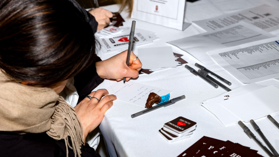 Brown students grab pens and cards at a table outside an athletics game to write personal letters to city residents.