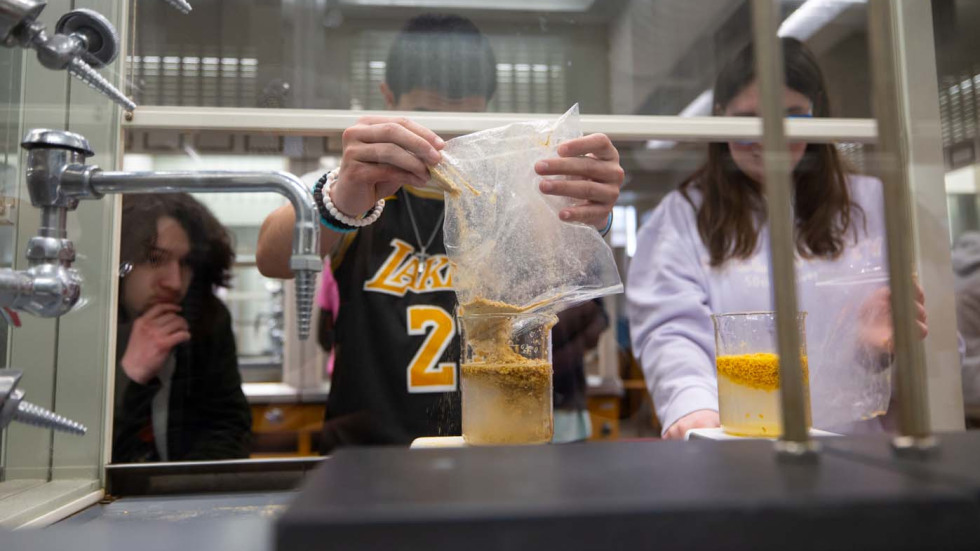 students look at a container of material under a fume hood