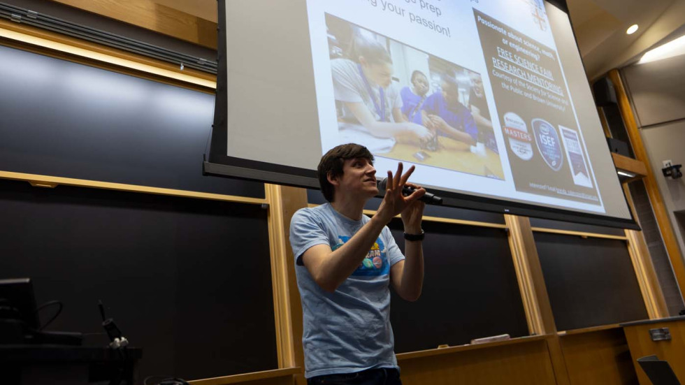 a person in front of a large screen speaking into a microphone