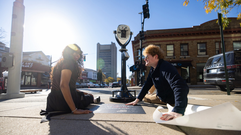Rishika Kartik and Daniel Solomon sit on the sidewalk as they finish installing the Blind Urban Subject