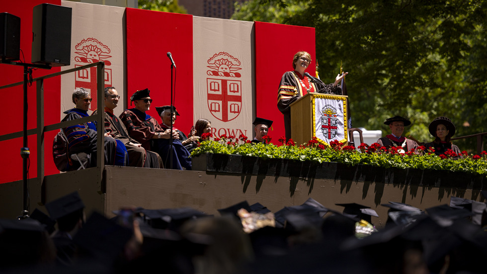 President Paxson speaking on stage at Commencment with flowers in front of podium