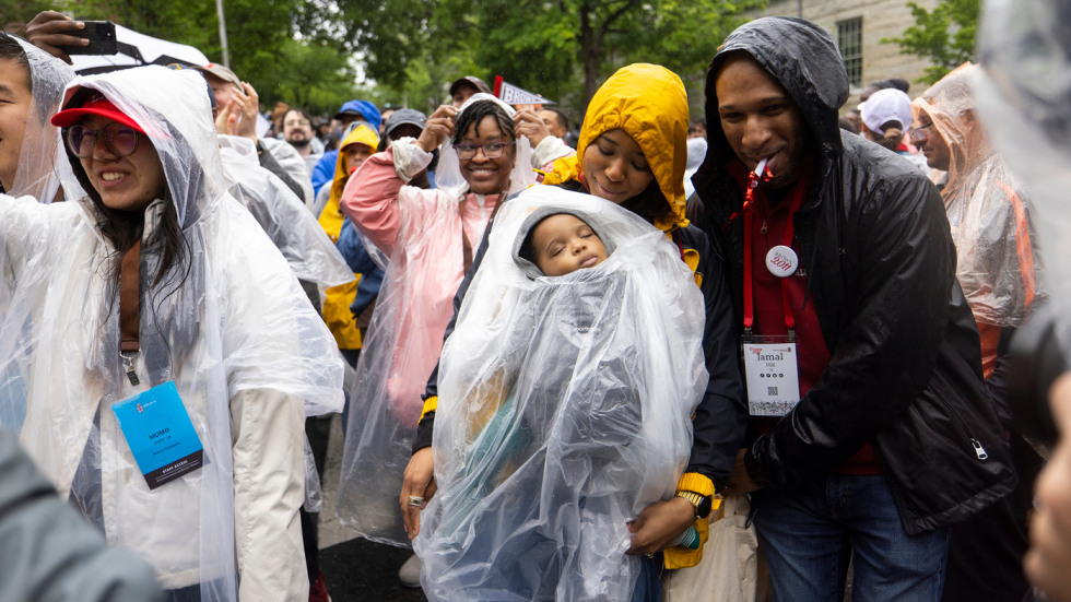 a mother holds a sleeping baby as alumni and students cheer around her