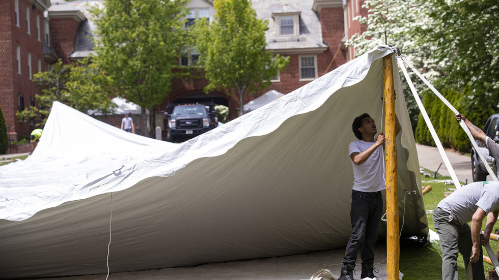 A worker start to erect one half of a giant white tent by securing a pole on one end. 