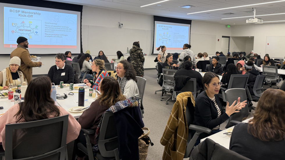 Mentors join students and families at a mentor kick off event, talk at tables. 