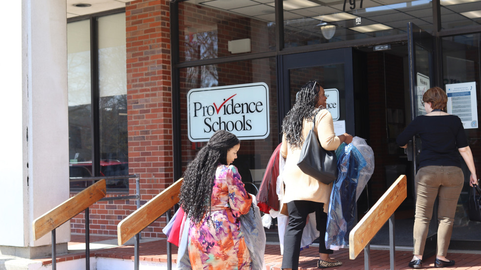 Brown staff members carry dresses and bags of donations into the front entrance of the Providence Public School District. 