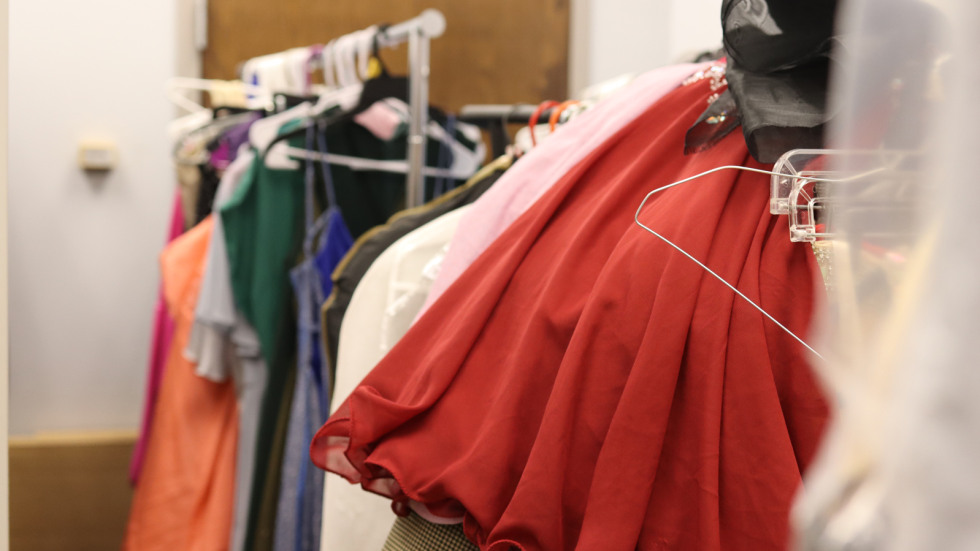 Racks of colorful dresses are hung on a garment rack in a supply closet room where donations are kept. 