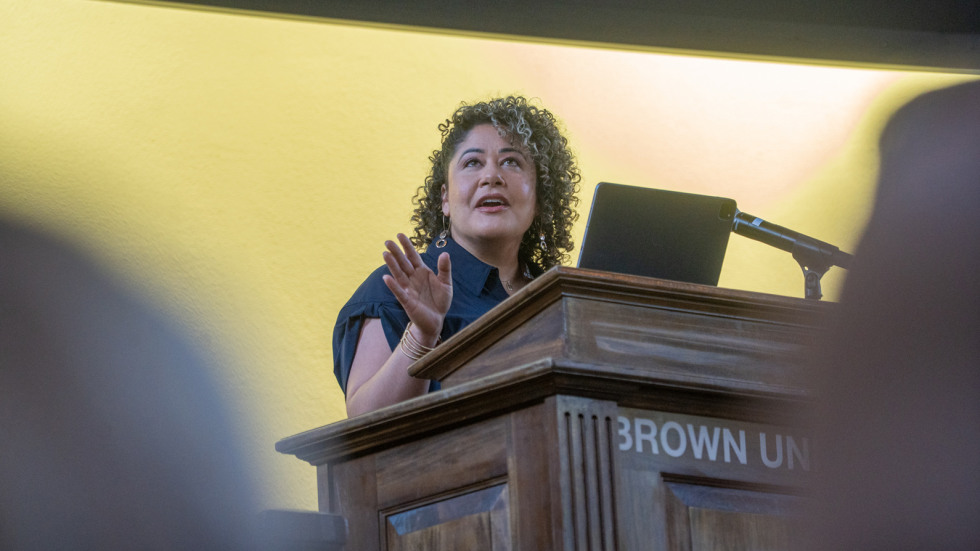 Rhode Island business owner Shirley Moore speaks at a podium to a crowd of brown staff and small business owners.