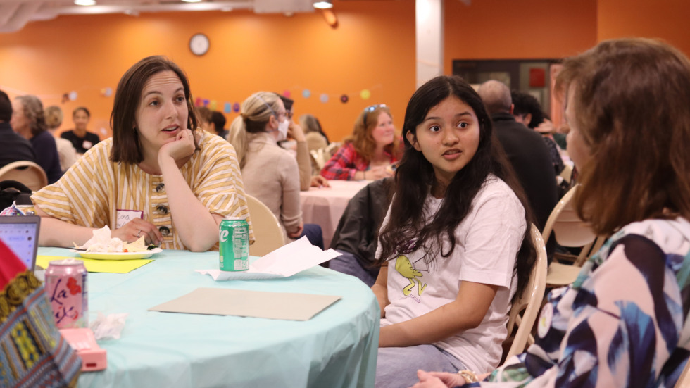 a Brown researcher and Providence teen look on to another at a table listening to her speak