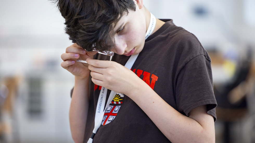 A pre-college students looks through a microscope at a fossil. 