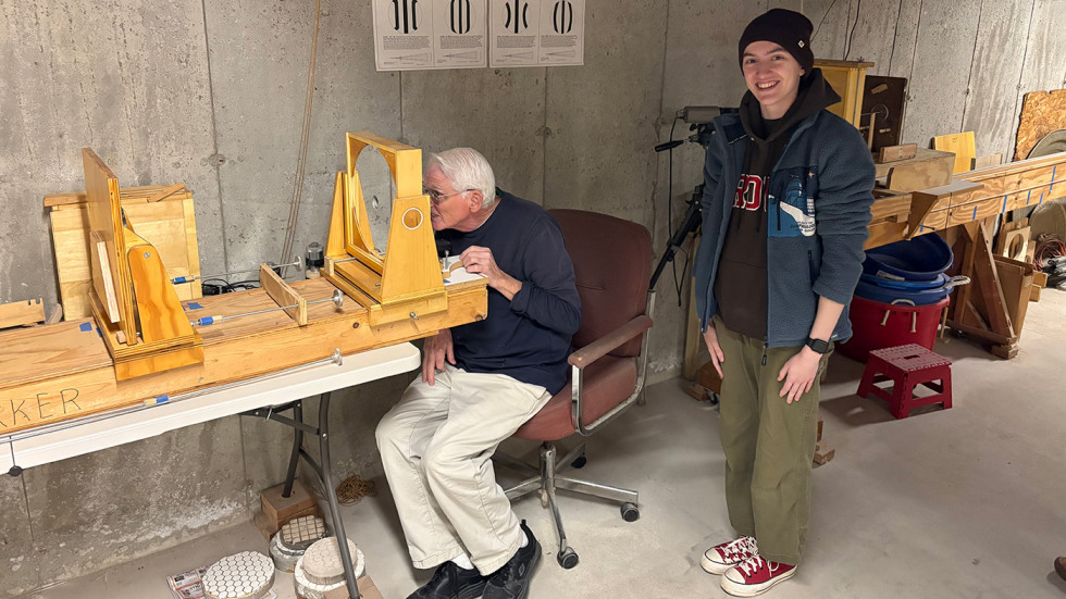 one person standing while another person looks through an optical testing device