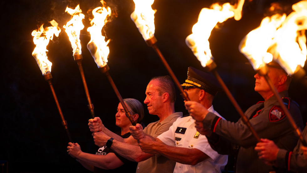 Brown community members stand shoulder to shoulder holding torches of fire preparing to ignite the waterfire art installation 