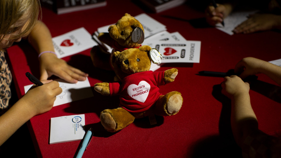 kids sign cards and draw pictures at an arts and crafts table with a teddy bear wearing a brown loves providence tshirt
