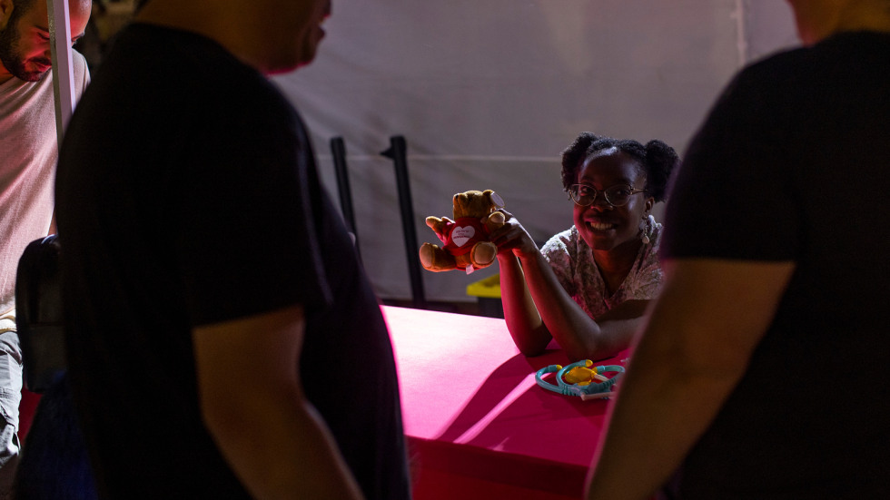 a brown medical students smiles as participants pass by the table where she holds supplies to engages kids in giving teddy bears checkups