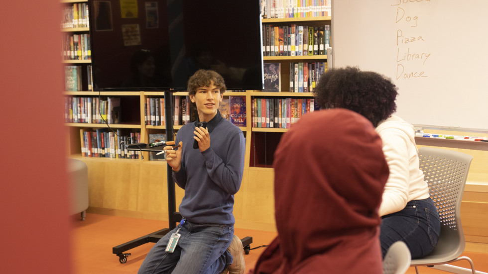 Dunn looks on to the students he teaches, surrounded by students in a circle in the library. 