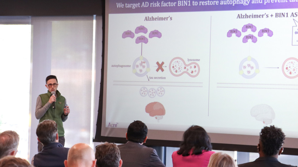 A researcher stands in front of a large powerpoint projection talking to a crowd.