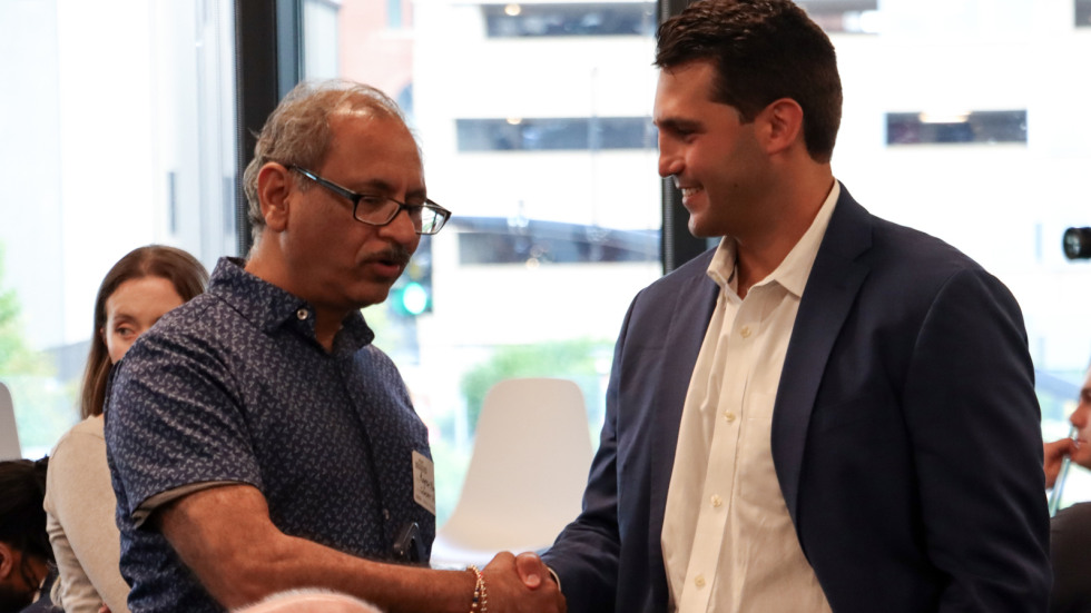 Two men smile and handshake among a group of professionals after the pitch competition.
