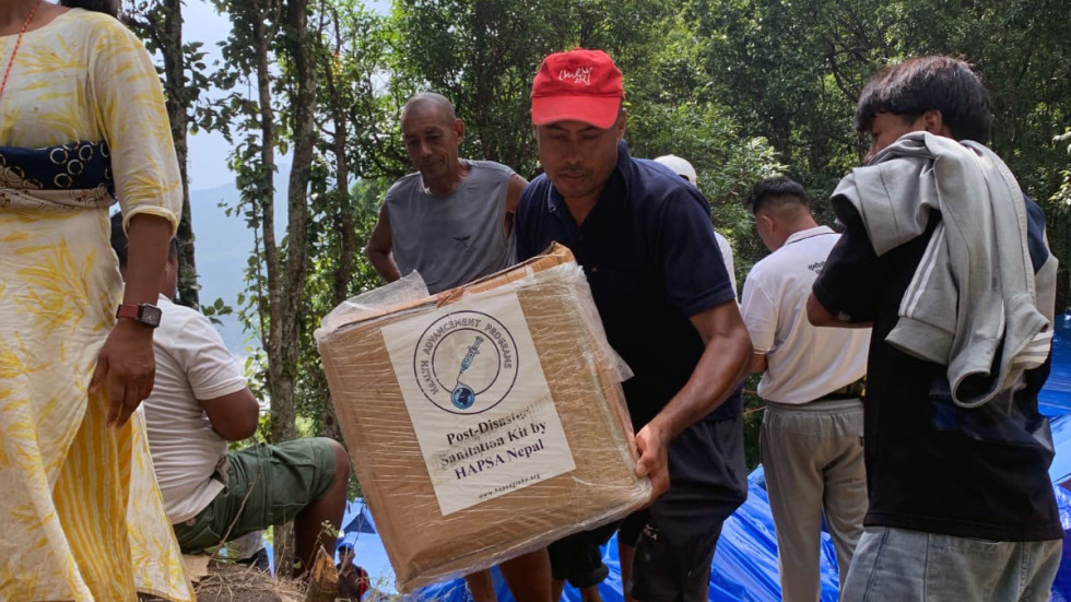 HAPSA volunteer carrying box with sanitation kits that says "Post-Disaster Sanitation Kits by HAPSA Nepal"