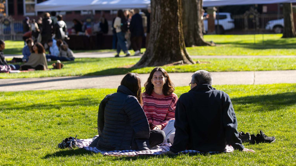 Brown student sits a blanker on the College Green with family. 