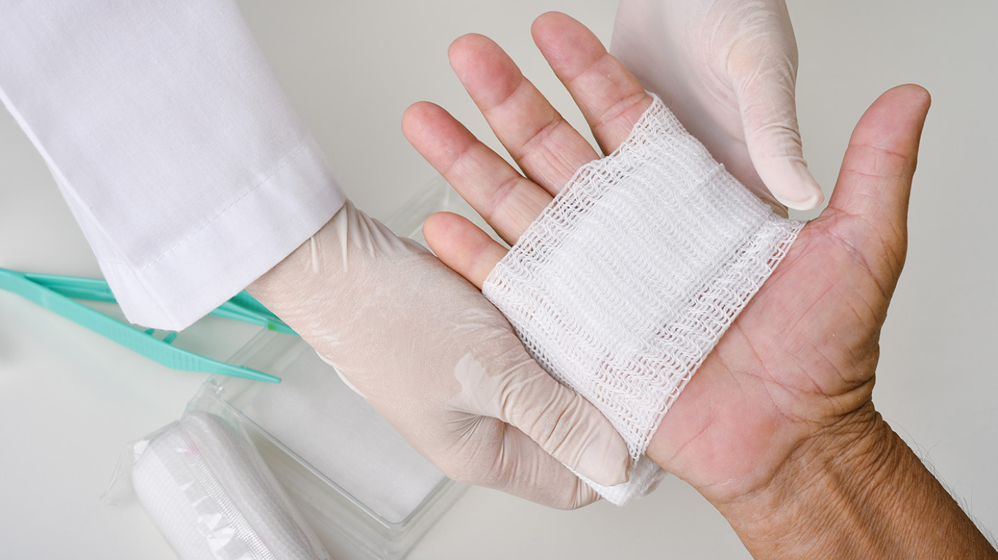 Gloved hands applying a gauze bandage to a patient's palm