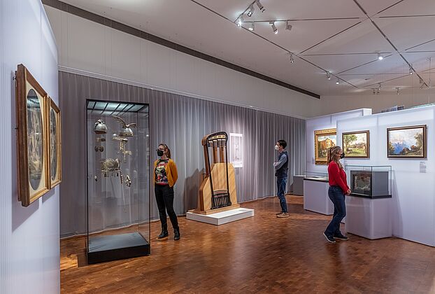 people looking at paintings, books and musical instruments inside a museum