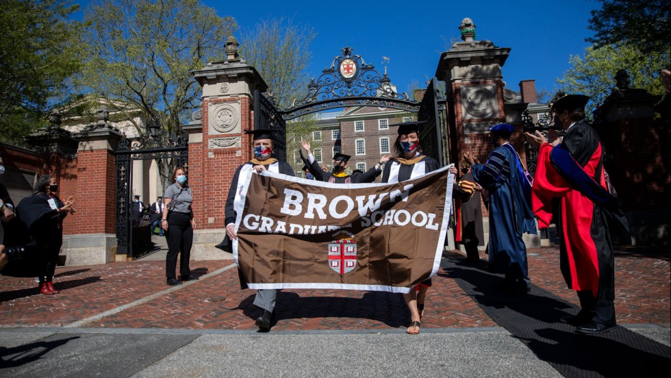 students holding a graduate school banner and walking through Van Wickle Gates