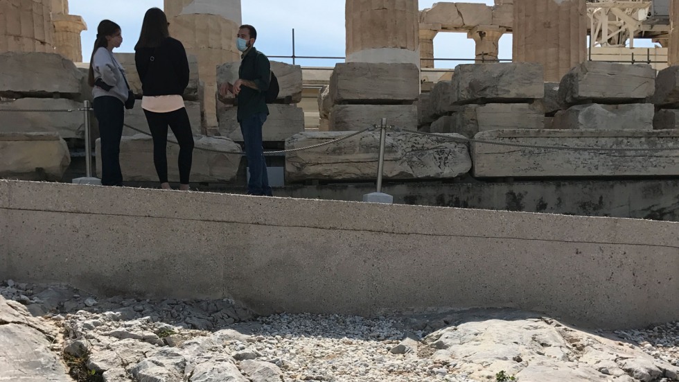 Three people gathered near ancient columns on a new concrete walkway