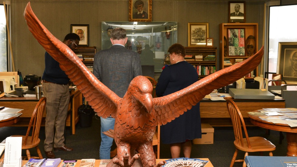 carved wooden eagle in front of three people looking down at a table