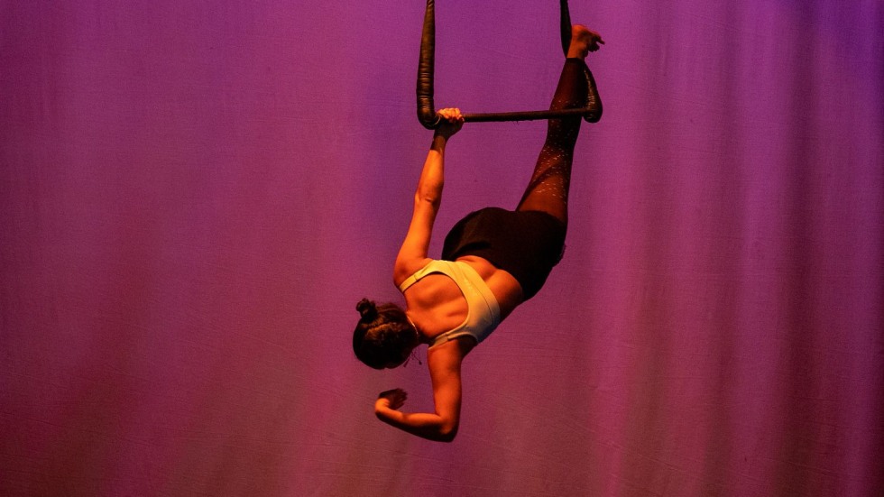 woman hanging from a trapeze in front of a pink curtain
