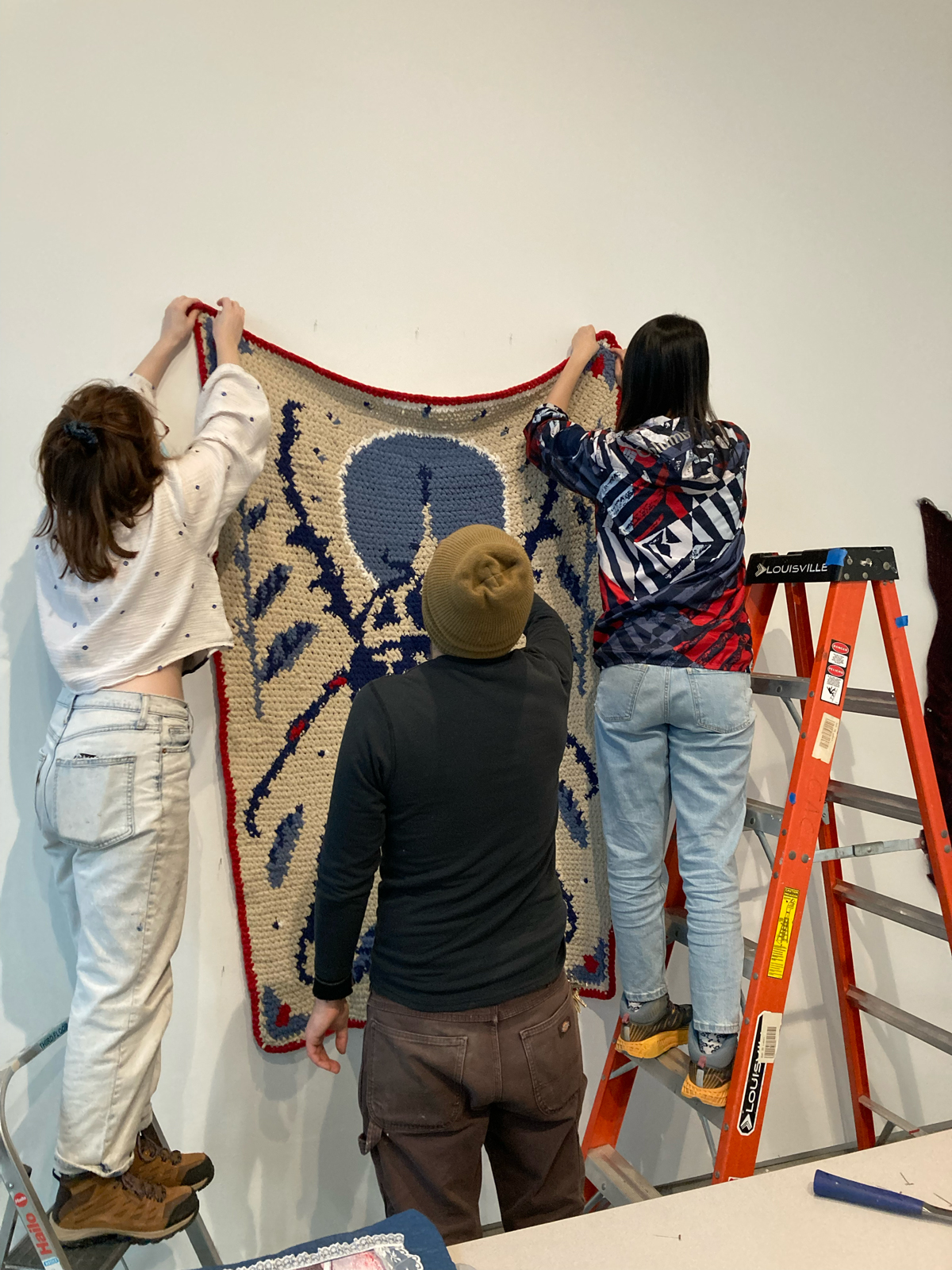 three people hang a textile artwork on the gallery wall